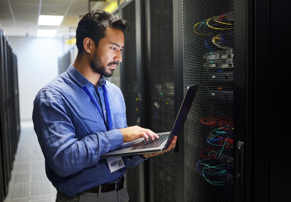 Asian man in computer server room with laptop